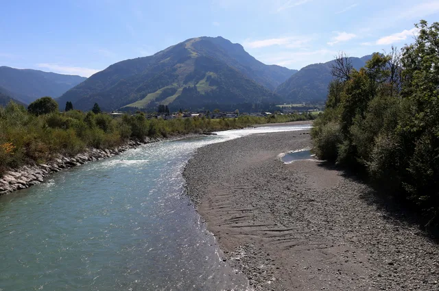 Fluss mit Kiesufer, Berge im Hintergrund und Ufervegetation