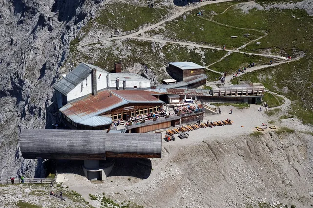 Alpine Berghütte mit Terrasse, Liegen und Wanderwegen an felsiger Berglandschaft.