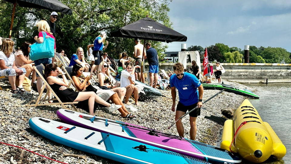 Wassersportausrüstung, Liegestühle und Gäste am Kiesufer in Kressbronn