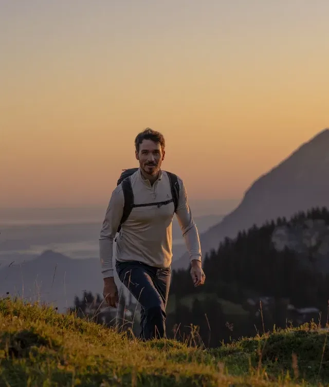 Mann mit Rucksack wandert bergauf bei Sonnenuntergang.