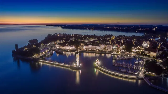 Luftaufnahme Lindau-Hafen bei Sonnenuntergang mit beleuchteten Gebäuden und Booten