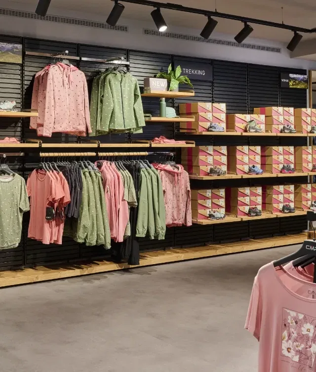 Outdoor-Shop-Regalwand mit pinken und grünen Jacken, Schuhen und Kartonboxen