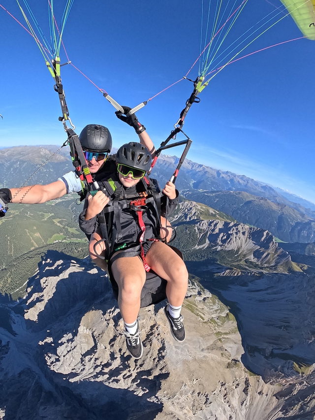 Tandem-Gleitschirmflug über hochalpiner Felslandschaft unter blauem Himmel