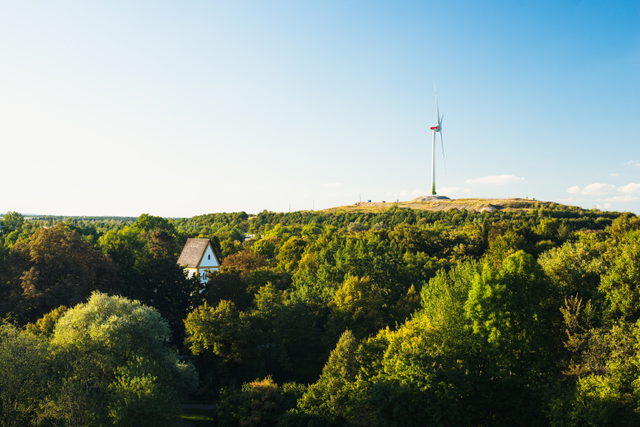 Fröttmaninger Berg mit Windrad und Kirche am bewaldeten Hang