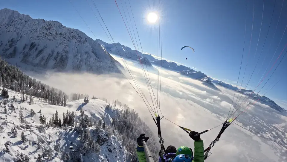 Tandemflug über verschneiten Berghängen und einer Wolkendecke