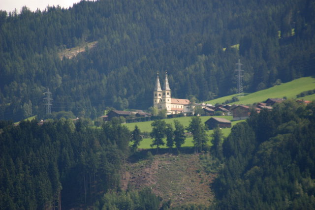 Kirche und grüne Wiesen am bewaldeten Hang oberhalb des Inntals