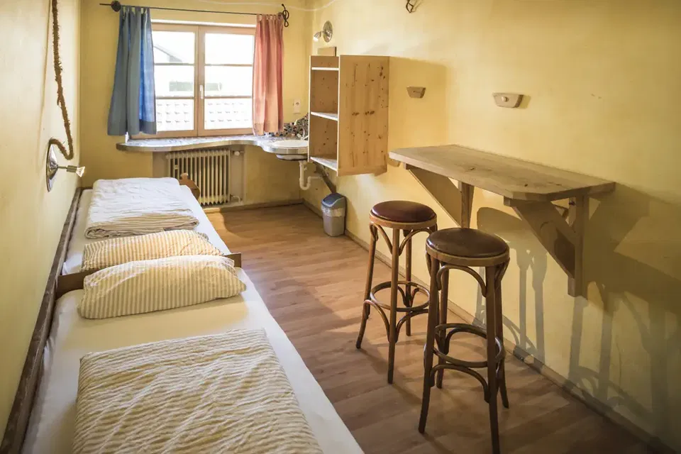 Zimmer Lagune mit zwei Einzelbetten, Holztisch, Hockern und Waschbecken am Fenster