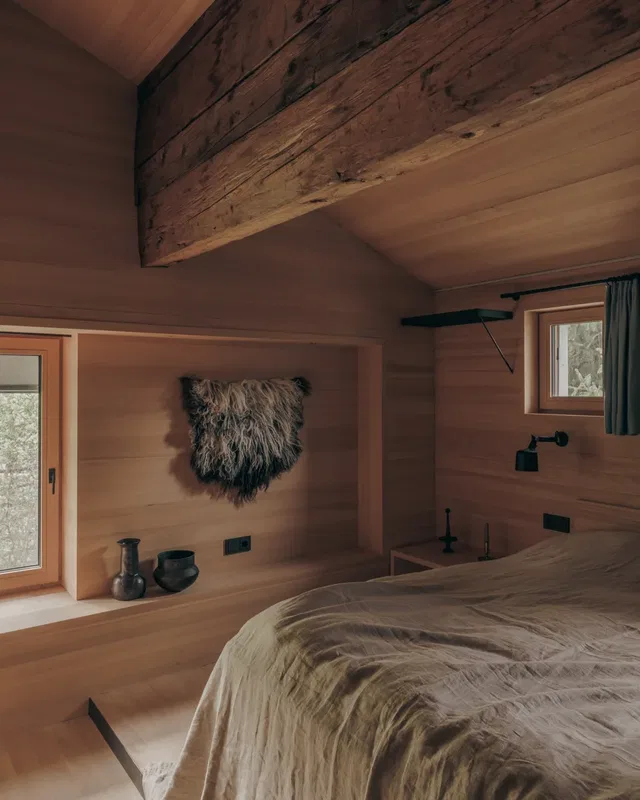 Gemütliches Schlafzimmer aus Holz mit freigelegter Balken-Decke, Bett und Fellwanddeko.