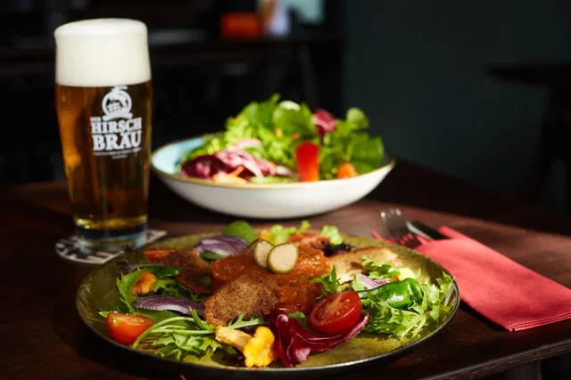 Salat mit Fleischstücken und Bierglas Hirschbräu auf Esstisch