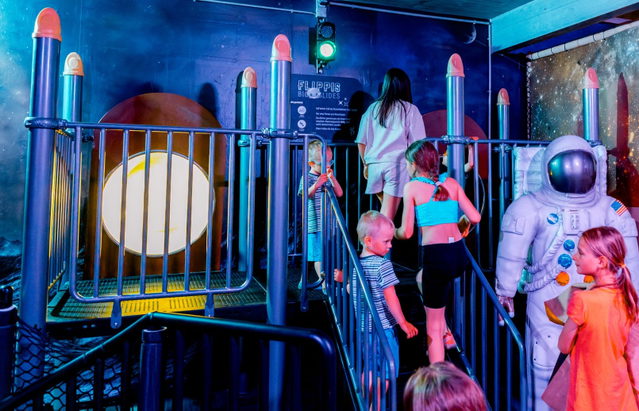 Familien in einer blau beleuchteten Weltraum-Ausstellung neben einem Astronautenmodell