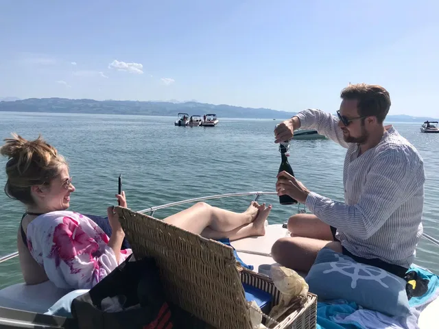 Paar auf Boot am Wasser, Mann öffnet Sektflasche, Frau sitzt entspannt