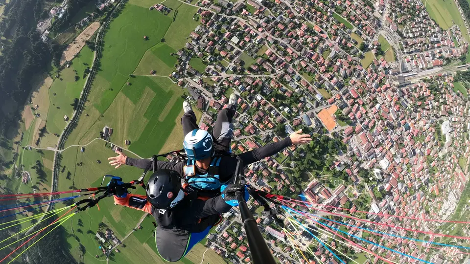 Pilot und Passagier beim Tandemflug über einer Ortschaft und grünen Wiesen.