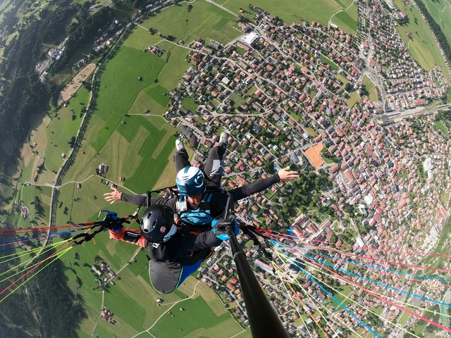 Pilot und Passagier beim Tandemflug über einer Ortschaft und grünen Wiesen.