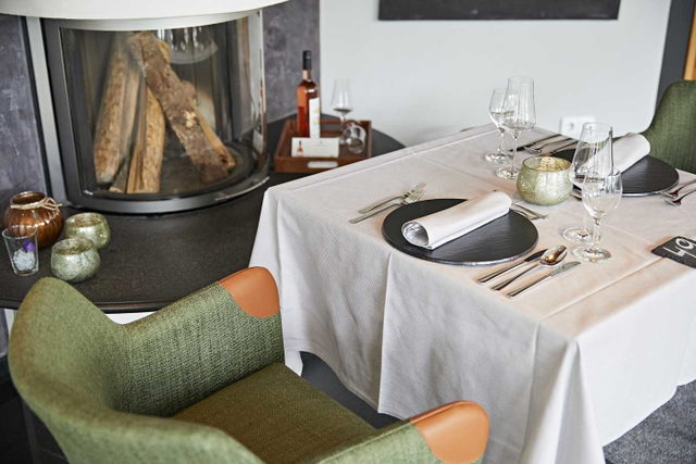 Gedeckter Tisch mit grünen Sesseln neben dem Kamin im Restaurant Rosenstock