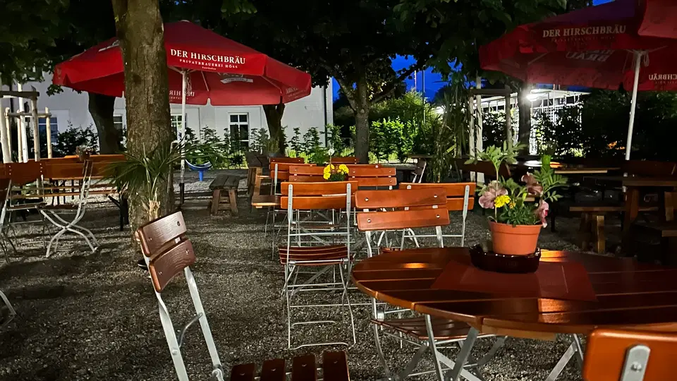 Biergarten des Hotels unter Bäumen mit roten Sonnenschirmen
