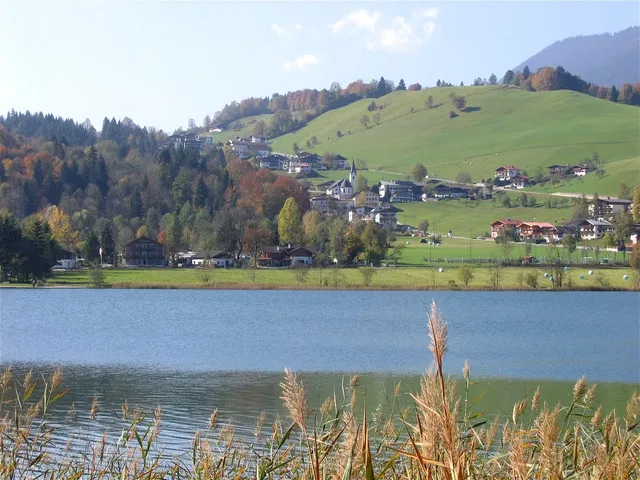 Landschaft mit See, Hügeln und Dorf im Hintergrund