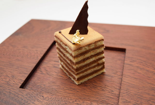 Dessertschnitte mit Goldblatt und Schokoladenspitze auf Holzbrett