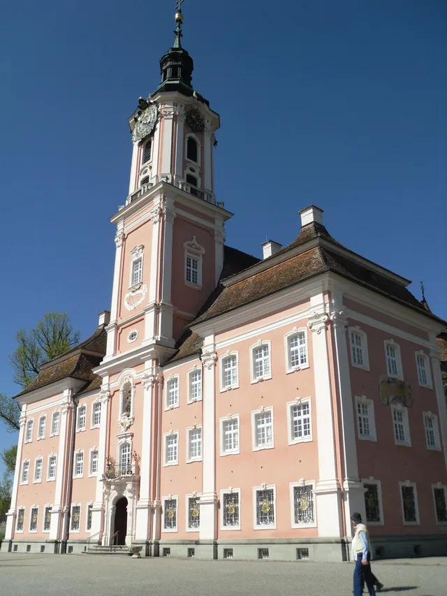 Barockes Gebäude in Birnau mit pinkfarbener Fassade und Turm, vor blauem Himmel.