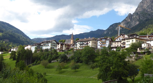 Teseros Häuser und Kirchturm über begrünten Hängen vor den Bergen des Fleimstals