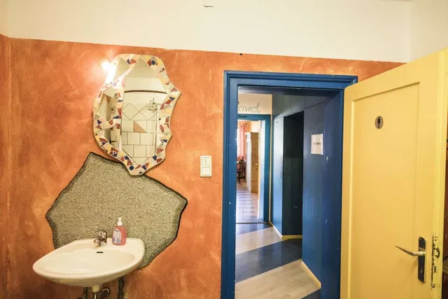 Waschbecken vor orange Wand, mosaikspiegel, blauer Türrahmen geöffnet zum Flur