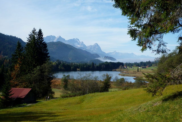 Blick über den Geroldsee mit Wiesen, Heustadeln und Bergen im Hintergrund