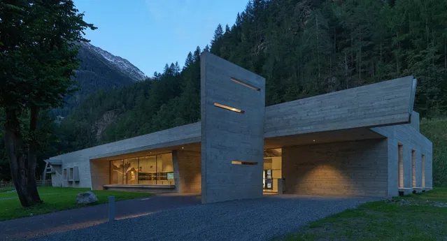 Moderne Betonarchitektur vor Wald und Bergen am Abend