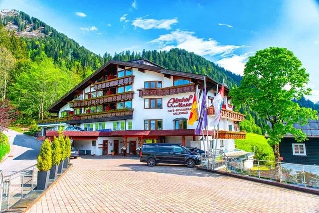 Mehrstöckiges Chalet-Hotel mit Holzbalustraden, Parkplatz vor dem Eingang, umgeben von Wald und Berg
