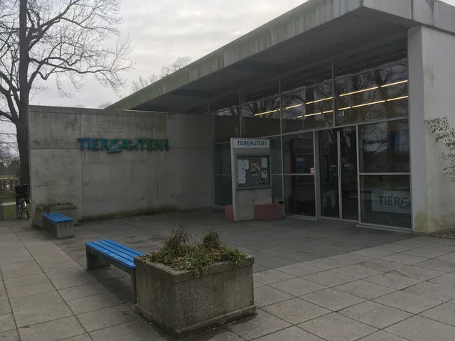 Eingang des Tiergartens mit gläserner Fassade und blauen Bänken