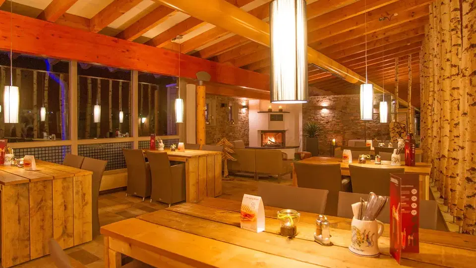 Gemütliches Restaurant mit Holzbalken, Birkenstützen und warmem Licht.
