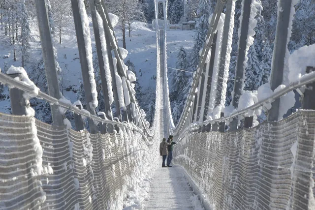 Zwei Gäste auf der verschneiten Highline179 zwischen vereisten Tragseilen.