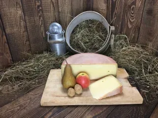 Käselaib und Käsestück mit Obst auf einem Holzbrett