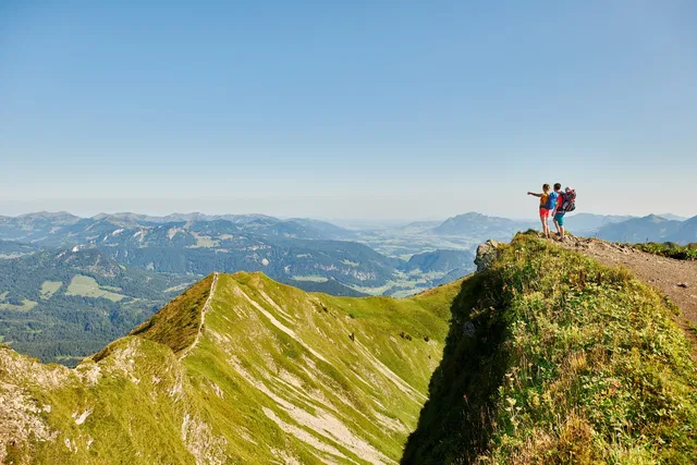 Zwei Wanderer mit Rucksack am Rand eines Bergkamms schauen ins Tal.