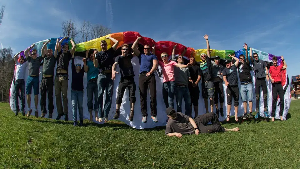 Kursgruppe vor einem bunten Gleitschirm auf einer Wiese.