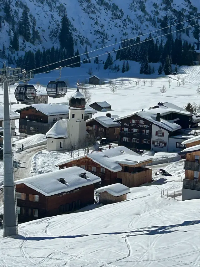 Skigebiet mit Schnee, Holzhäusern, Kirche und Gondelbahn im Winter