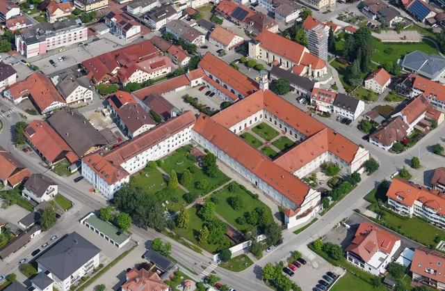 Luftaufnahme eines quadratischen Klosterkomplexes mit roten Ziegeldächern und Innenhofgärten.