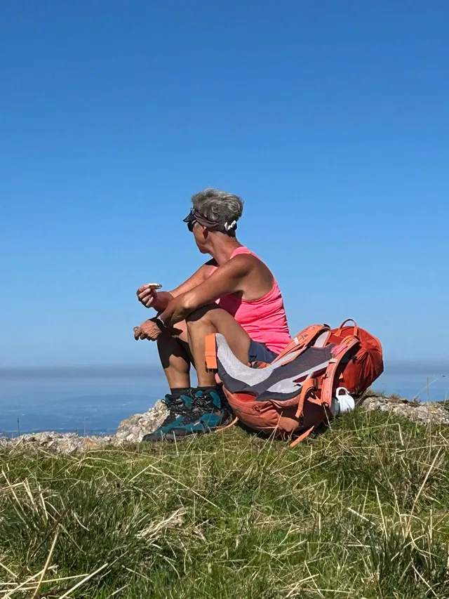 Rast auf einem Grashang mit Rucksack und weitem Ausblick.
