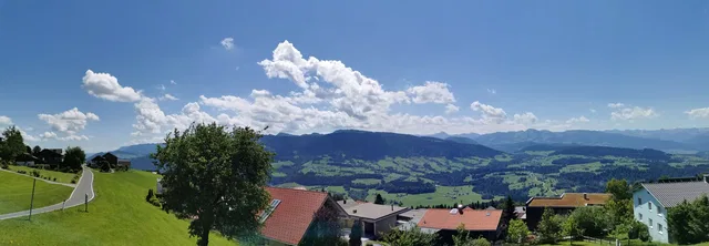 Panorama einer malerischen Hügellandschaft mit Häusern, grünem Gras und blauem Himmel.