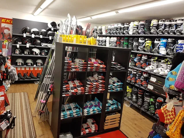 Skiausrüstung in einem Geschäft: Helme, Skischuhe und Skier auf Regalen und Wandaufbauten.