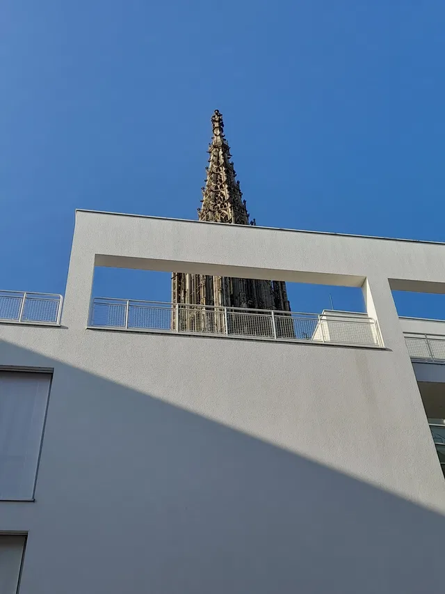 Gotische Kirchturmspitze hinter einem weißen Gebäude