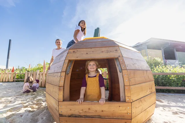 Kinder am runden Holzspielhaus auf dem Rapunzel-Spielplatz