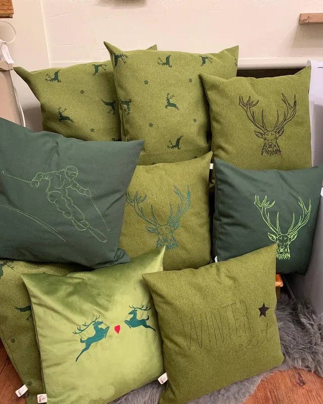 Grüne Kissen mit bestickten Tier- und Wintermotiven.