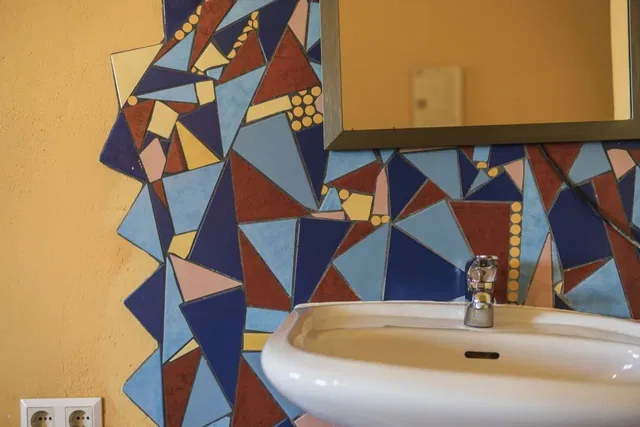 Bunte Geometrie-Mosaikfliesen an einer Badezimmerwand neben einem Waschbecken und Spiegel.