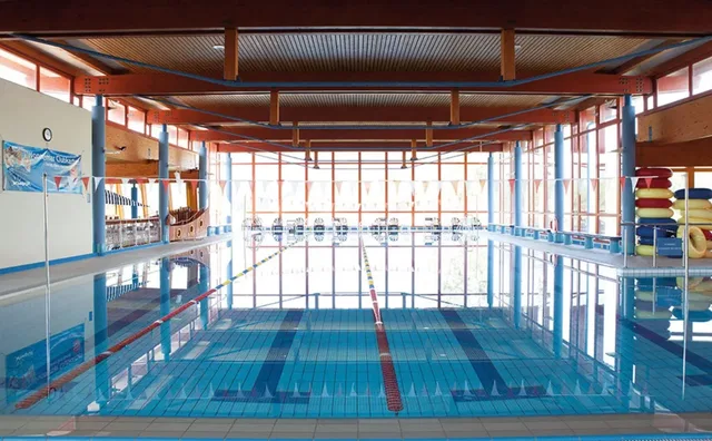 Innenpool in einer Halle mit Bahnen, Holzdecke und Seitenausrüstung am Rand.