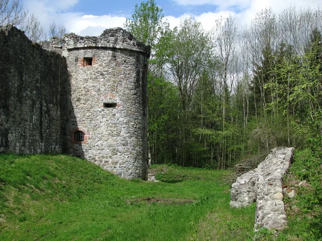 Verfallener runder Stein Turm neben Grüngras und Baumreihe