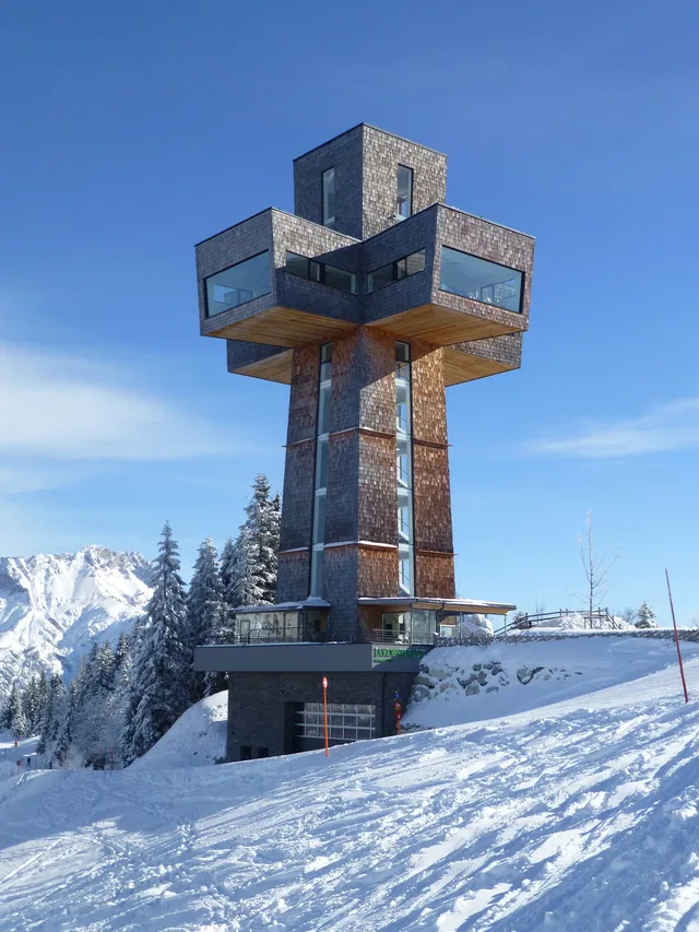 Moderne Turmstruktur aus Stein auf verschneitem Berggelände bei blauem Himmel
