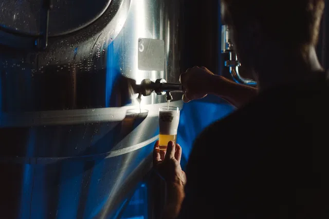 Person zapft Bier aus einer Edelstahl-Fassstation in einer Dampfbierbrauerei in ein Glas
