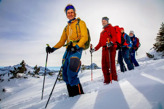 Gruppe von Wanderern mit Stöcken im Schnee in bergiger Winterlandschaft.