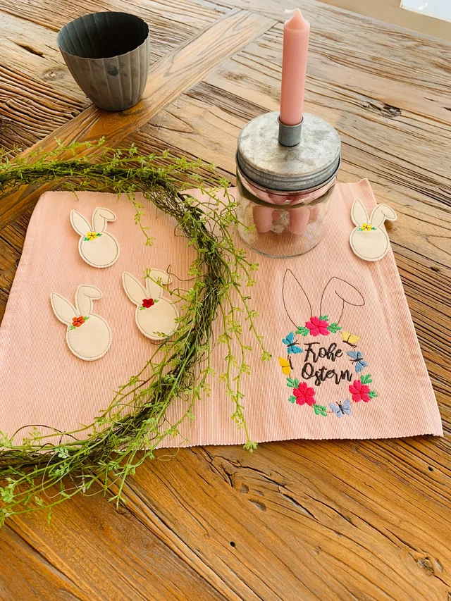 Osterdekoration mit Hasenanhängern, Zweigen und rosa Kerze auf einem Holztisch.
