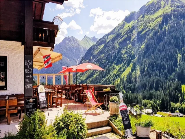 Terrasse des Starzelhauses mit roten Sonnenschirmen und Bergpanorama