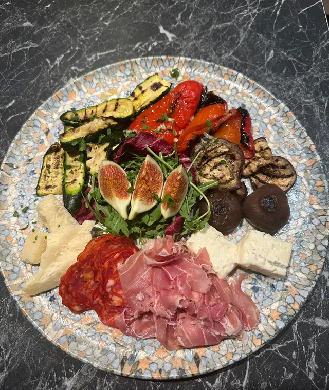 Bunte Käse- und Aufschnittplatte mit Feigen, gegrilltem Gemüse und Kräutern auf dekorativem Teller.